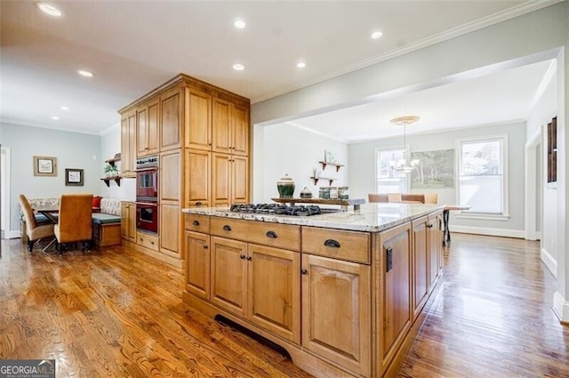 kitchen with wood finished floors, stainless steel gas stovetop, crown molding, multiple ovens, and a chandelier