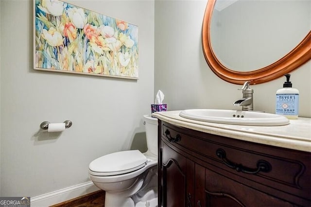 bathroom with vanity, toilet, wood finished floors, and baseboards