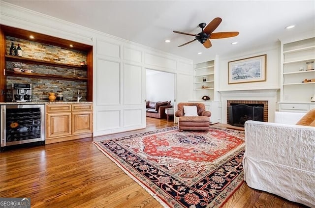 living area with built in shelves, wood finished floors, wine cooler, bar, and a brick fireplace