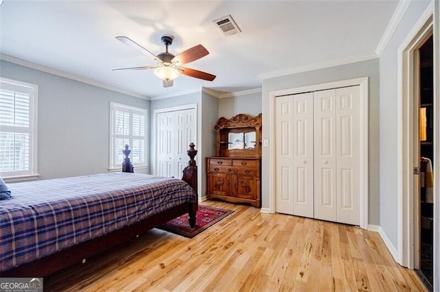 bedroom with visible vents, two closets, crown molding, baseboards, and light wood-style flooring