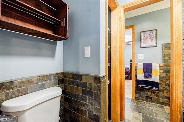 half bathroom with wainscoting, toilet, and tile walls