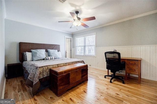 bedroom with ceiling fan, a wainscoted wall, light wood finished floors, and ornamental molding