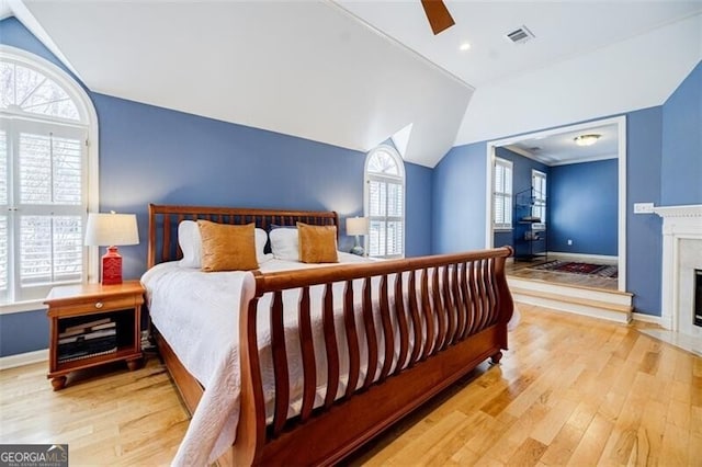 bedroom with light wood finished floors, visible vents, baseboards, lofted ceiling, and a ceiling fan