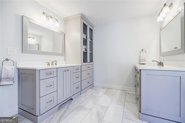 full bath featuring two vanities, baseboards, marble finish floor, and a sink