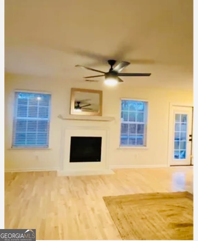 unfurnished living room featuring a fireplace, baseboards, a ceiling fan, and wood finished floors