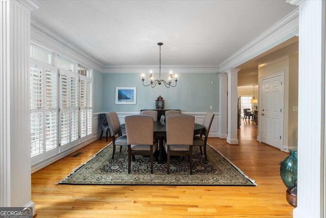 dining area featuring ornamental molding, a healthy amount of sunlight, wood finished floors, and ornate columns