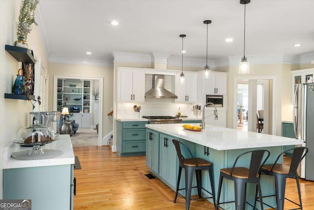 kitchen with a breakfast bar, wall chimney range hood, light countertops, and freestanding refrigerator