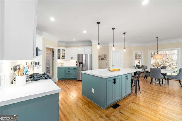 kitchen featuring light wood finished floors, hanging light fixtures, white cabinets, wall chimney range hood, and stainless steel fridge with ice dispenser