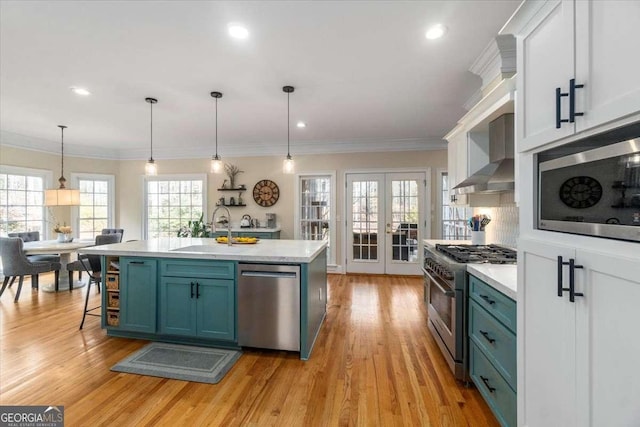 kitchen featuring french doors, stainless steel appliances, light countertops, a sink, and wall chimney range hood