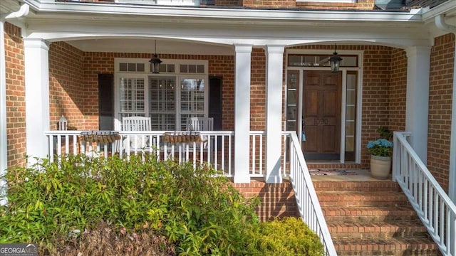 view of exterior entry with a porch and brick siding