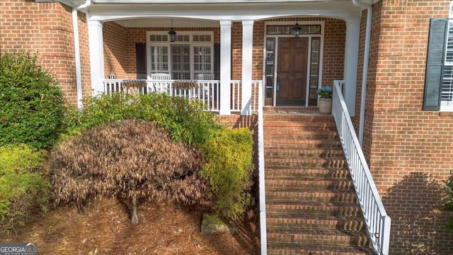 doorway to property featuring a porch and brick siding