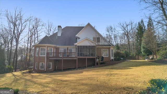 back of property with a yard, brick siding, a chimney, and a sunroom