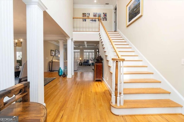 entrance foyer featuring wood finished floors, a towering ceiling, ornamental molding, stairway, and decorative columns