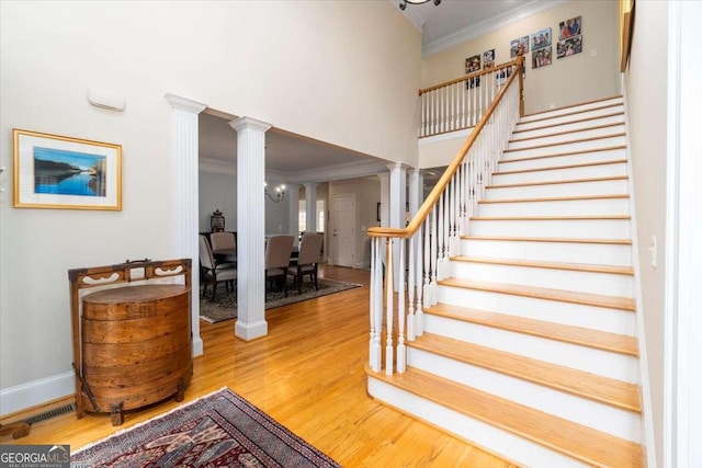 stairs featuring visible vents, a towering ceiling, ornamental molding, wood finished floors, and ornate columns