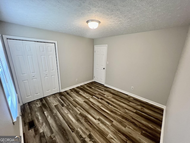 unfurnished bedroom featuring visible vents, dark wood-type flooring, baseboards, a closet, and a textured ceiling