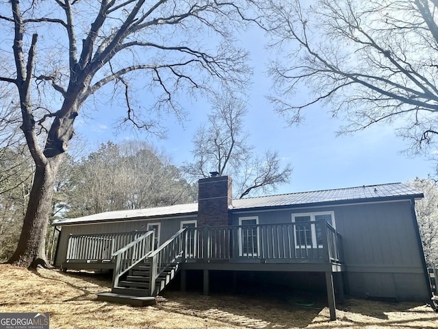 back of property with a wooden deck, a chimney, and metal roof