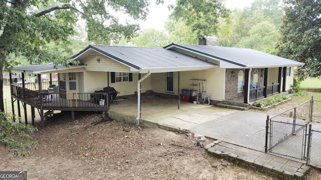 back of house with driveway, a chimney, metal roof, an attached carport, and a gate