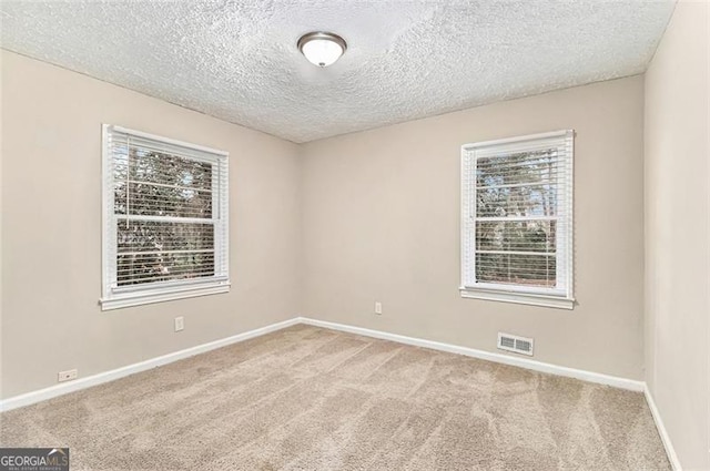 unfurnished room featuring a textured ceiling, carpet flooring, visible vents, and baseboards
