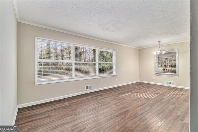 spare room with visible vents, an inviting chandelier, ornamental molding, wood finished floors, and baseboards