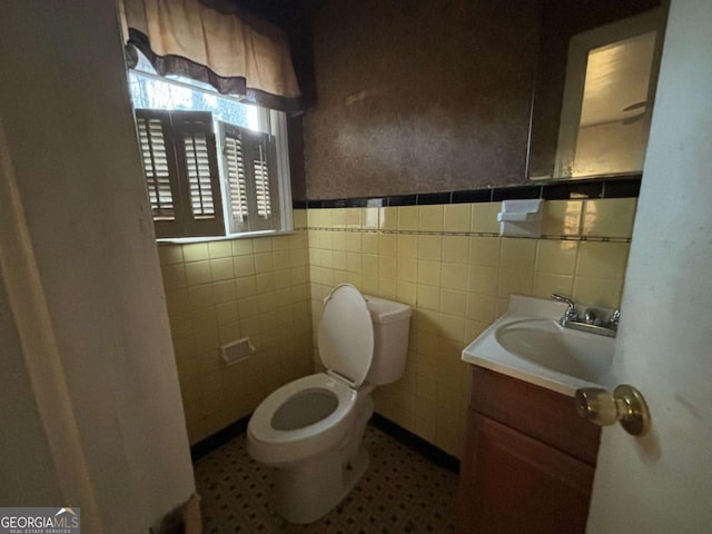 bathroom with wainscoting, vanity, toilet, and tile walls