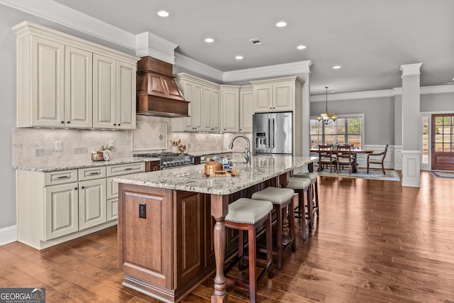 kitchen featuring a breakfast bar, custom exhaust hood, stainless steel appliances, a sink, and ornate columns