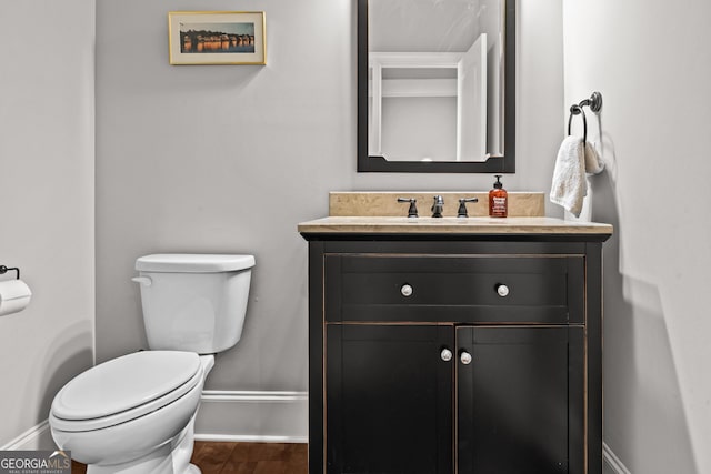 half bath with baseboards, vanity, toilet, and wood finished floors