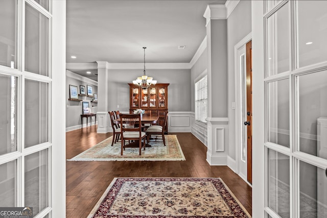 dining space with dark wood-style floors, ornamental molding, a decorative wall, and a notable chandelier