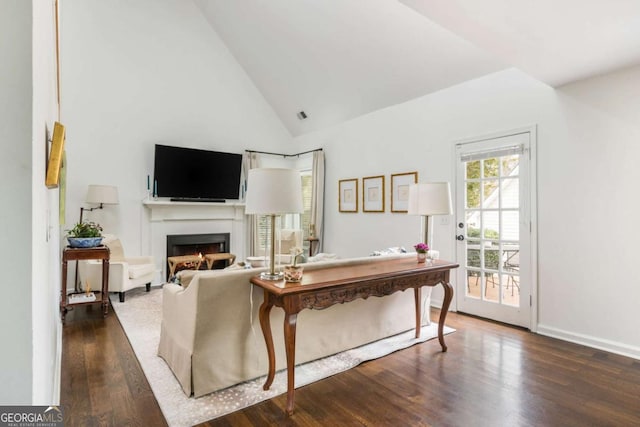 living room with high vaulted ceiling, a lit fireplace, baseboards, and wood finished floors