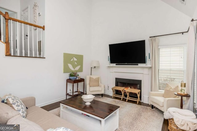 living area with a lit fireplace, high vaulted ceiling, wood finished floors, and baseboards