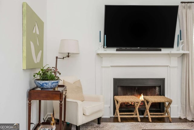 living area with a warm lit fireplace and wood finished floors