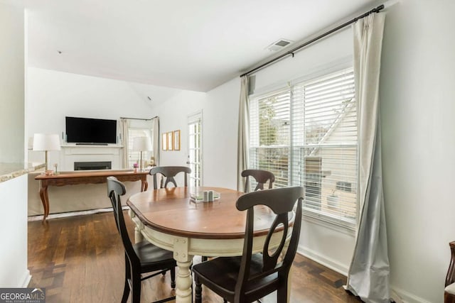 dining space featuring baseboards, visible vents, lofted ceiling, dark wood-type flooring, and a fireplace