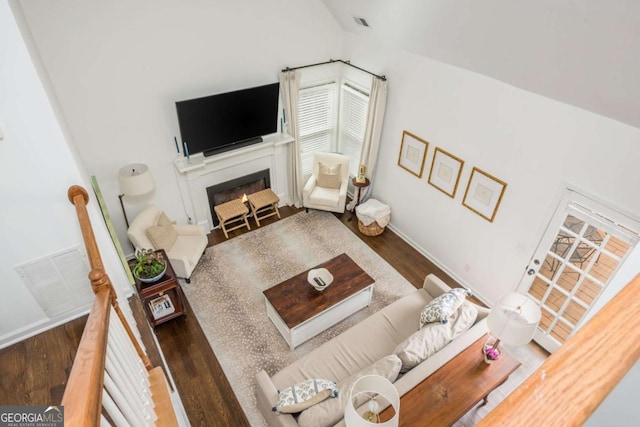 living room featuring a warm lit fireplace, baseboards, visible vents, wood finished floors, and vaulted ceiling