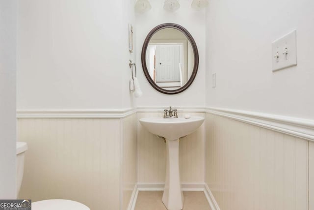 half bathroom with wainscoting, tile patterned flooring, and toilet