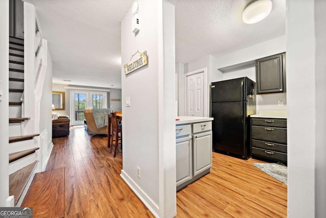 kitchen with light wood-type flooring, light countertops, a textured ceiling, and freestanding refrigerator