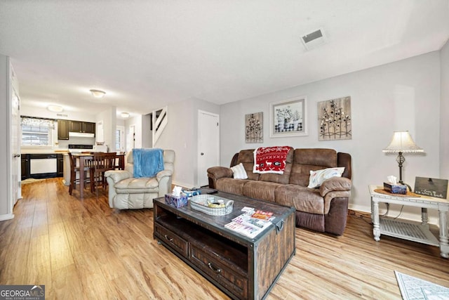 living room featuring visible vents, stairway, light wood-style flooring, and baseboards