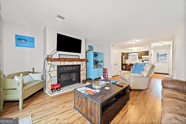 living area with light wood-type flooring, visible vents, a textured ceiling, and a stone fireplace