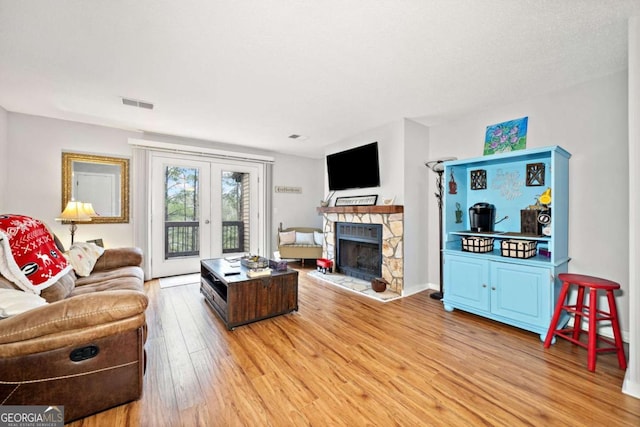 living room featuring french doors, visible vents, a fireplace, and light wood-style flooring