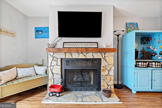 living room with a stone fireplace and wood finished floors