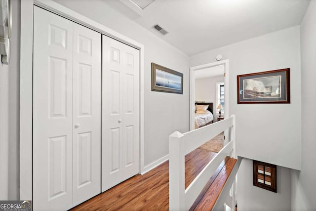 hallway with baseboards, visible vents, an upstairs landing, and wood finished floors