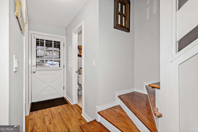 entryway with light wood-type flooring, stairway, baseboards, and a textured ceiling