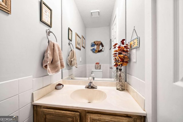 bathroom with a textured ceiling, vanity, and tile walls