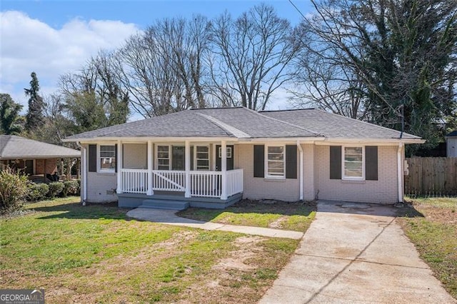 view of front of home featuring roof with shingles, covered porch, fence, a front lawn, and brick siding