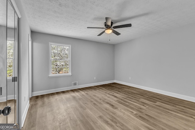 empty room with a ceiling fan, visible vents, baseboards, and wood finished floors