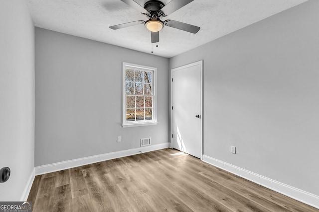 spare room featuring a textured ceiling, wood finished floors, visible vents, and baseboards