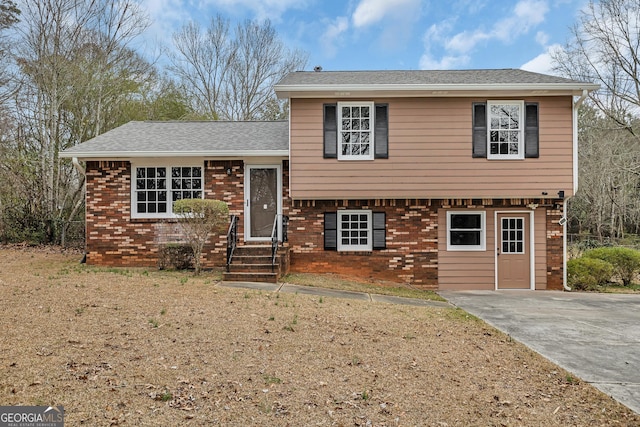 tri-level home with a shingled roof, brick siding, and driveway