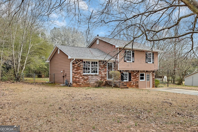 split level home featuring driveway, roof with shingles, fence, and brick siding