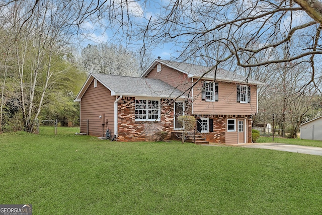 split level home featuring a shingled roof, brick siding, fence, and a front lawn