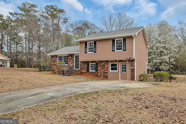 view of front facade featuring a shingled roof, brick siding, and driveway