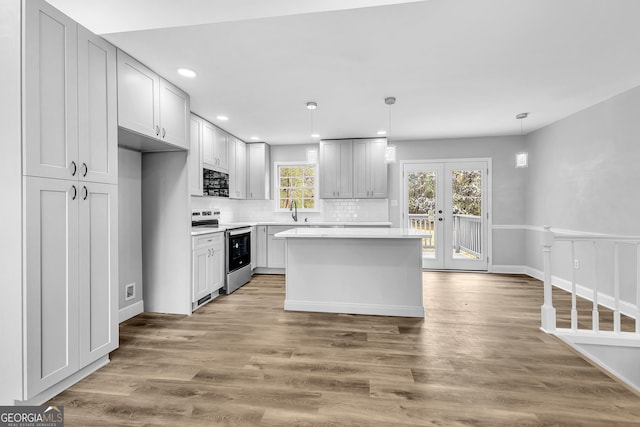 kitchen with light countertops, decorative backsplash, a sink, wood finished floors, and stainless steel electric range