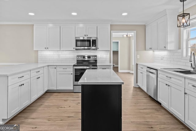 kitchen featuring white cabinets, a peninsula, stainless steel appliances, crown molding, and a sink